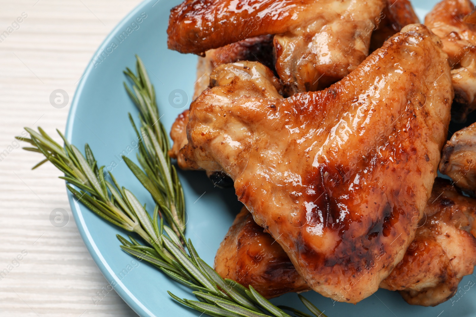 Photo of Plate with delicious fried chicken wings and sprig of rosemary on white wooden table, closeup