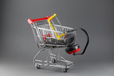 Photo of Small shopping cart with hacksaw, gloves and headphones on grey background