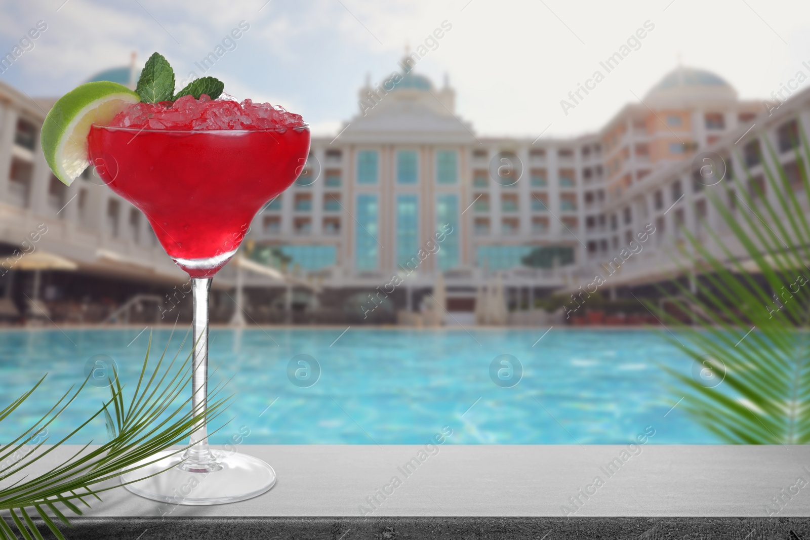 Image of Fresh alcoholic Margarita on grey stone table near outdoor swimming pool at resort, space for text