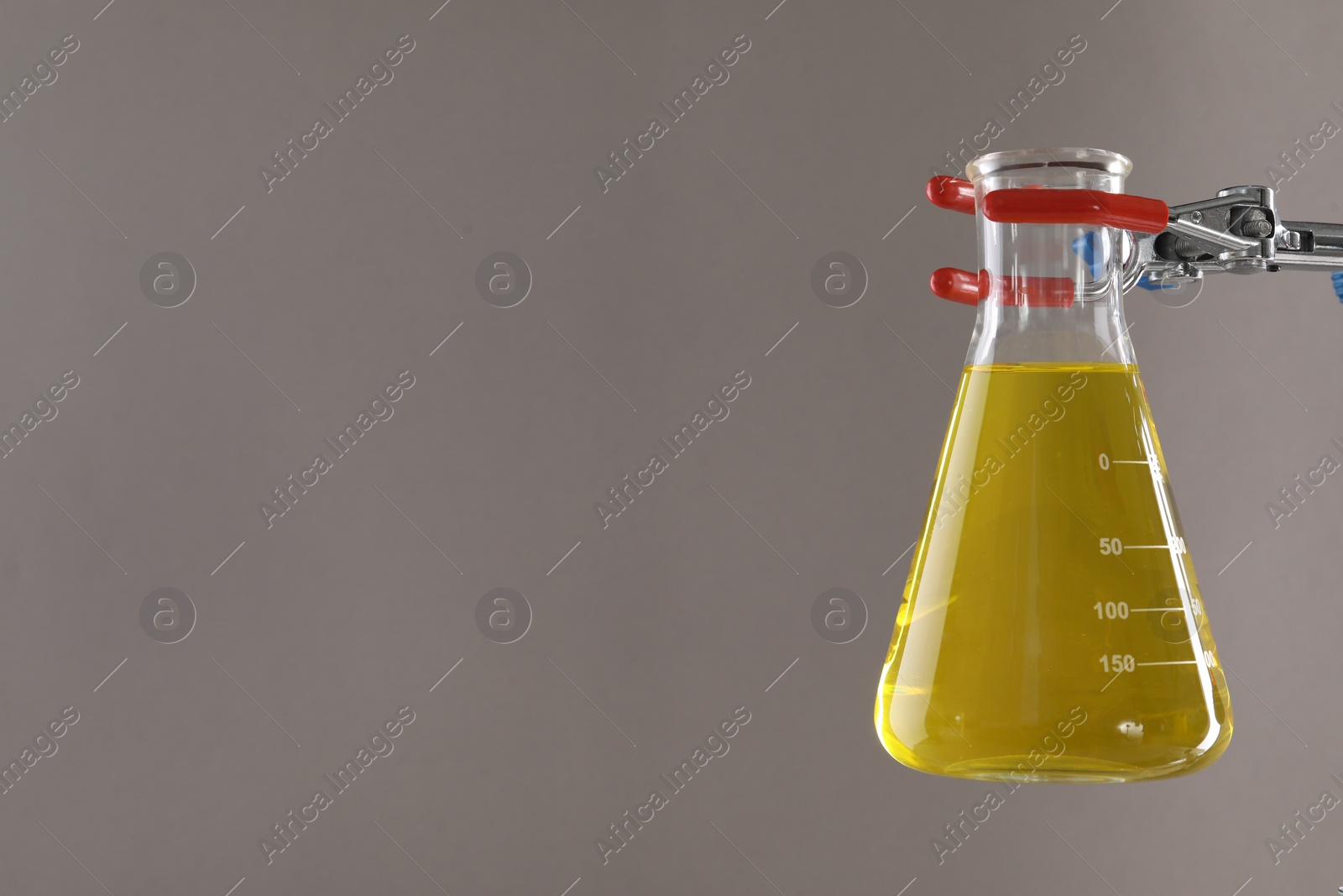 Photo of Retort stand and laboratory flask with liquid on light grey background, closeup. Space for text