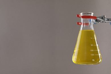 Photo of Retort stand and laboratory flask with liquid on light grey background, closeup. Space for text