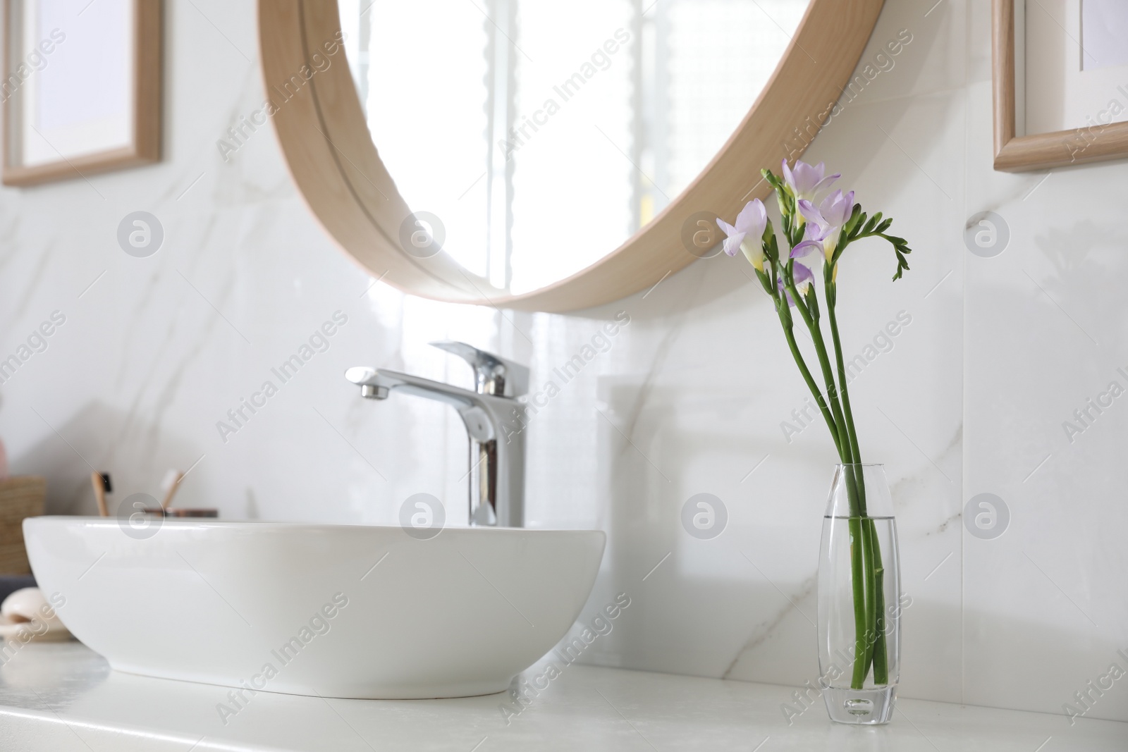 Photo of Beautiful violet freesia flowers on countertop in bathroom