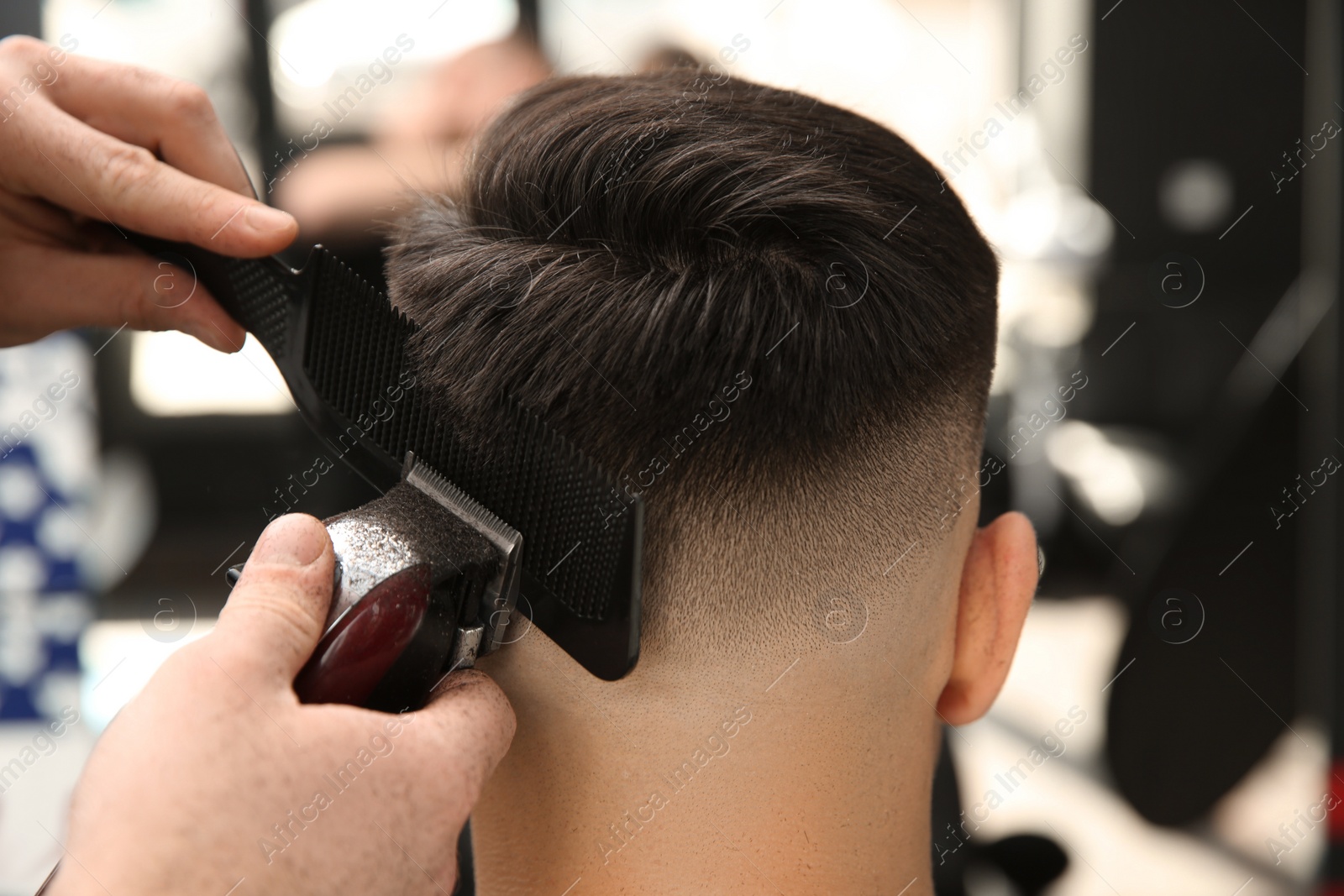 Photo of Professional barber making stylish haircut in salon, closeup