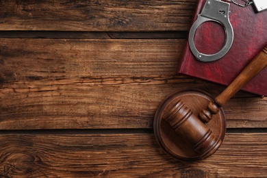 Flat lay composition with handcuffs and gavel on wooden table, space for text. Criminal law