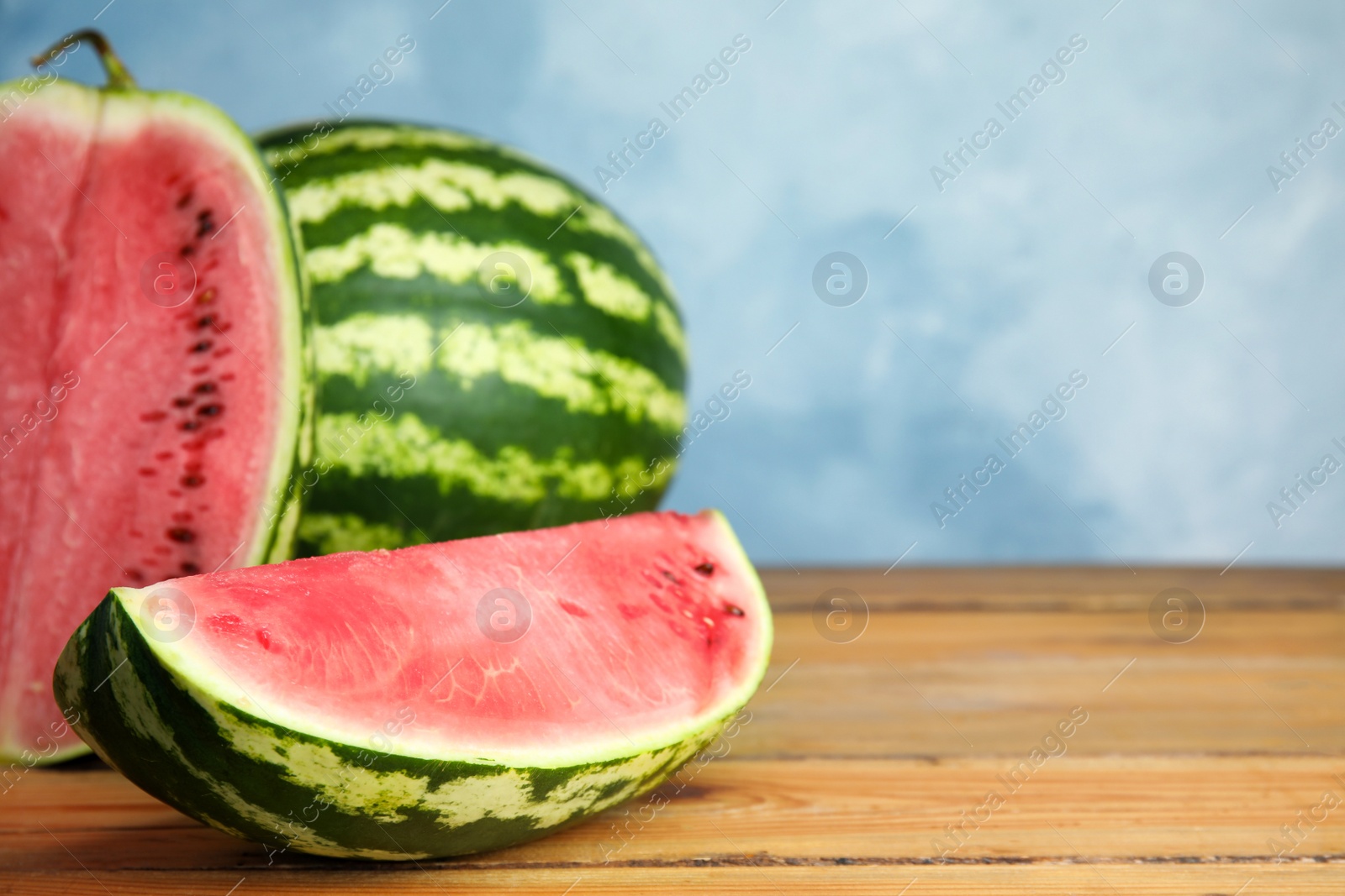 Photo of Yummy watermelons on wooden table near color wall, space for text