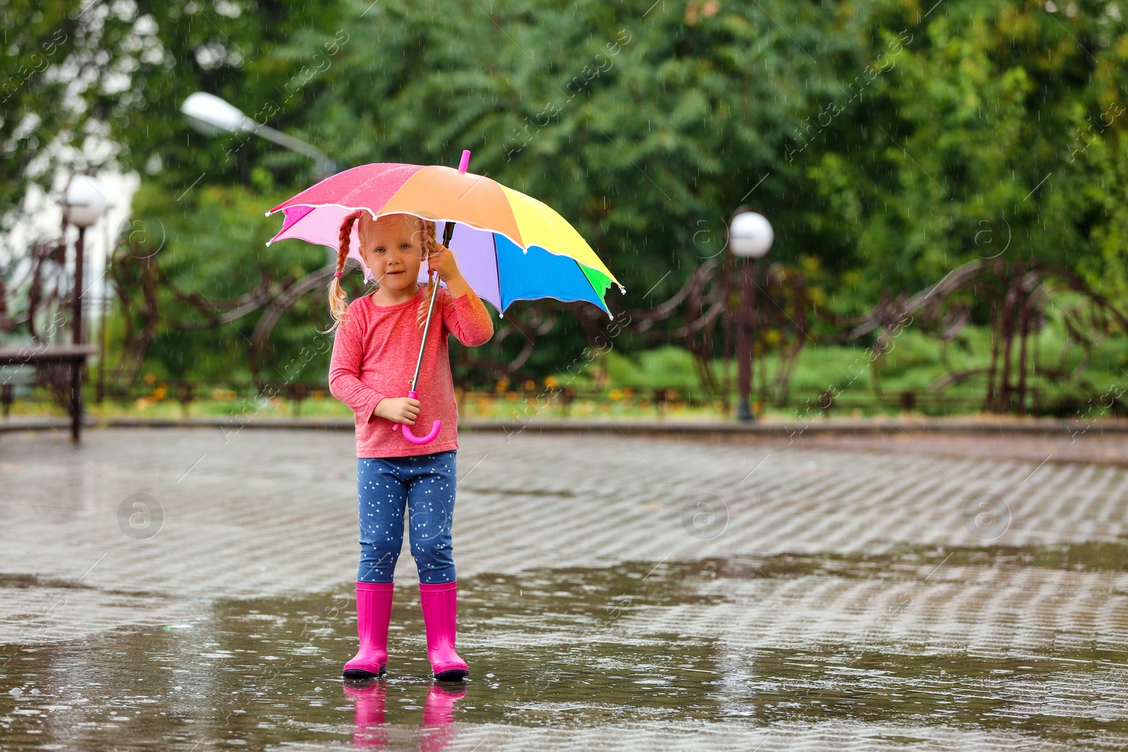 Photo of Cute little girl with bright umbrella under rain on street