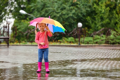 Cute little girl with bright umbrella under rain on street