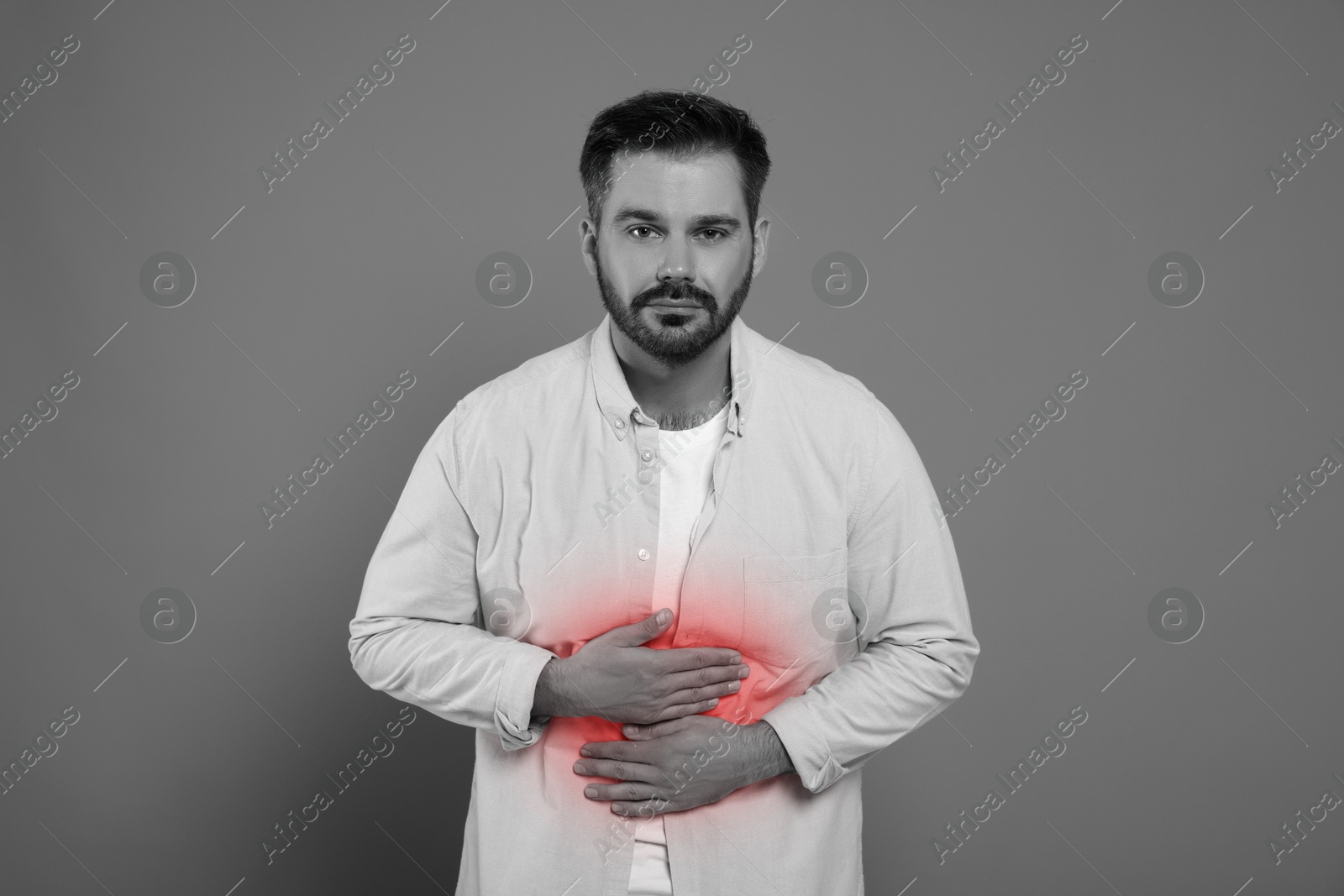 Image of Man suffering from abdominal pain on grey background. Black and white effect with red accent