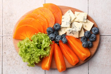 Delicious persimmon, blue cheese and blueberries on tiled surface, flat lay