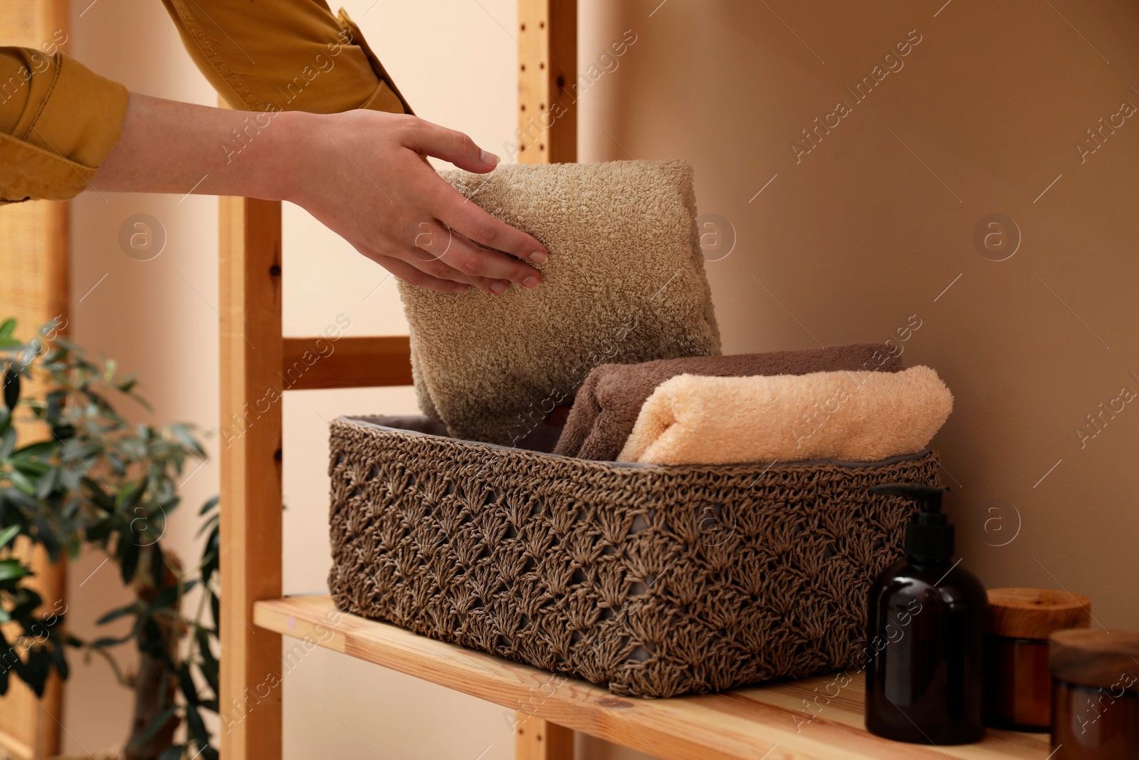 Photo of Woman putting towel into storage basket indoors, closeup