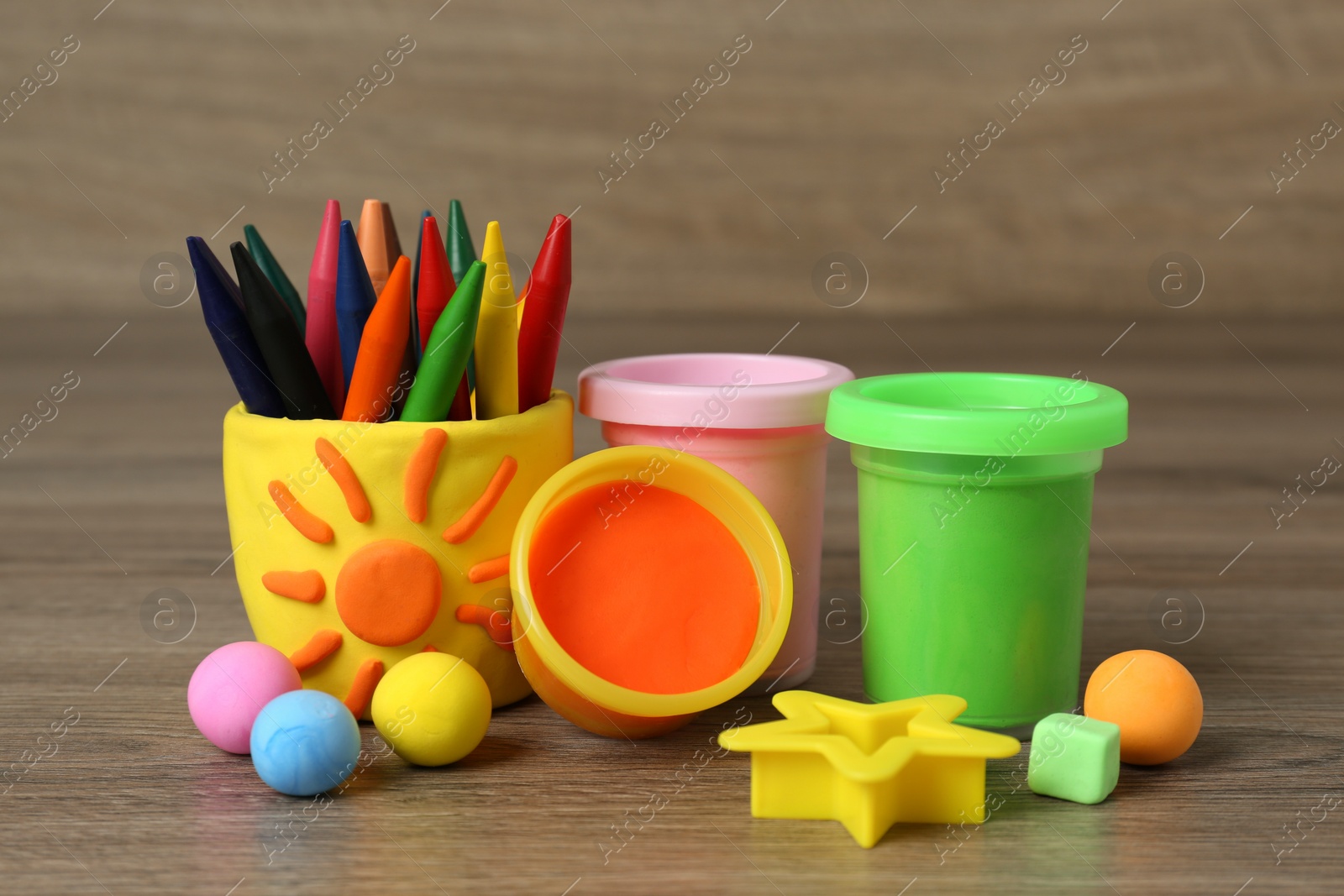 Photo of Set of bright play dough with mold and colorful pencils on wooden table