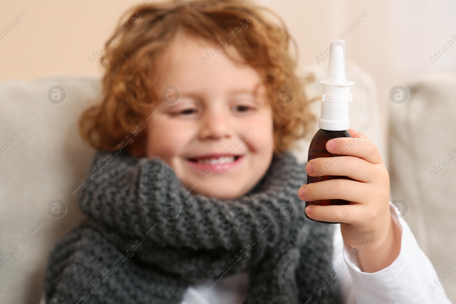 Photo of Cute little boy showing nasal spray indoors, focus on bottle