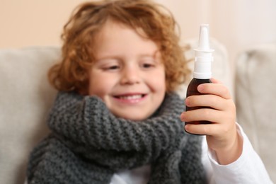Photo of Cute little boy showing nasal spray indoors, focus on bottle