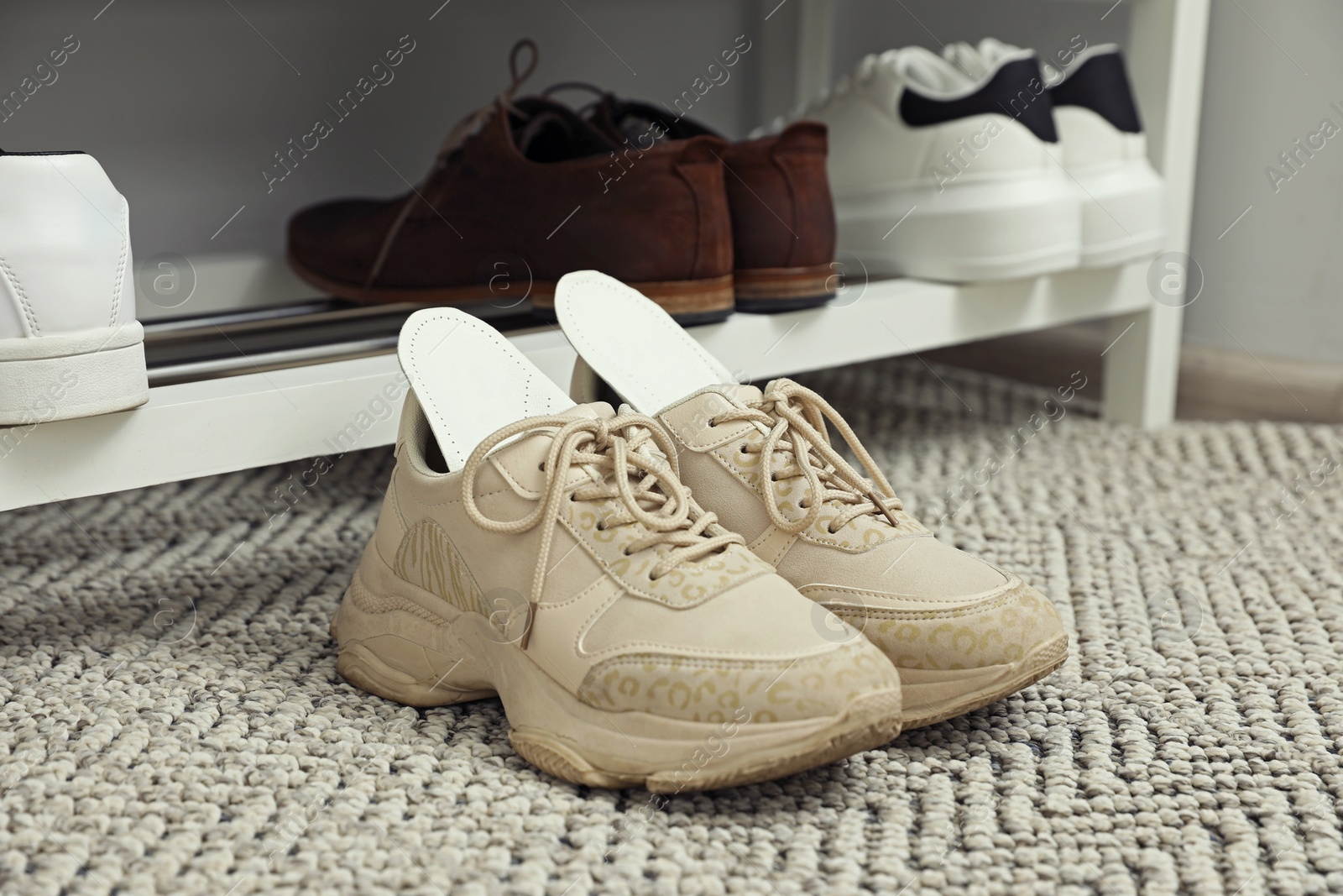 Photo of Orthopedic insoles in shoes on rug near rack, closeup