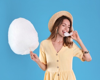 Photo of Happy young woman eating cotton candy on blue background