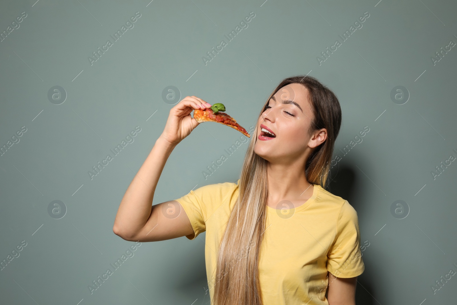 Photo of Attractive young woman with slice of delicious pizza on color background