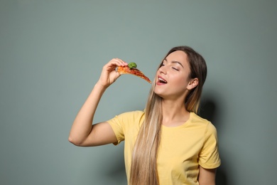 Attractive young woman with slice of delicious pizza on color background