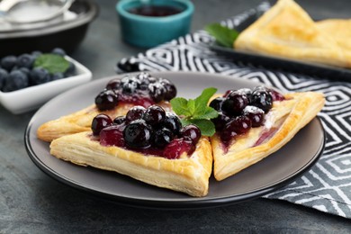 Fresh tasty puff pastry with sugar powder, jam, sweet berries and mint on grey table, closeup