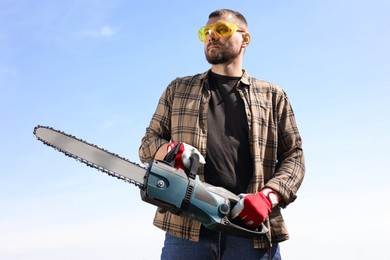 Man with modern saw against blue sky, low angle view