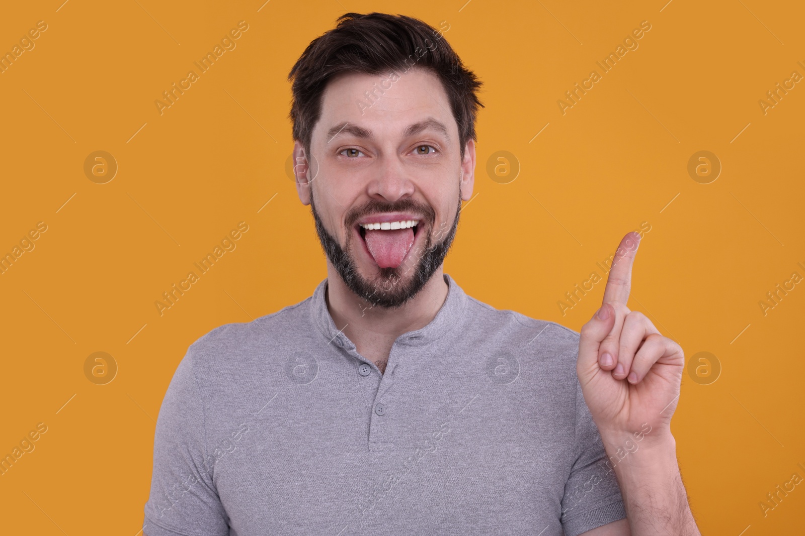 Photo of Happy man showing his tongue and pointing on orange background