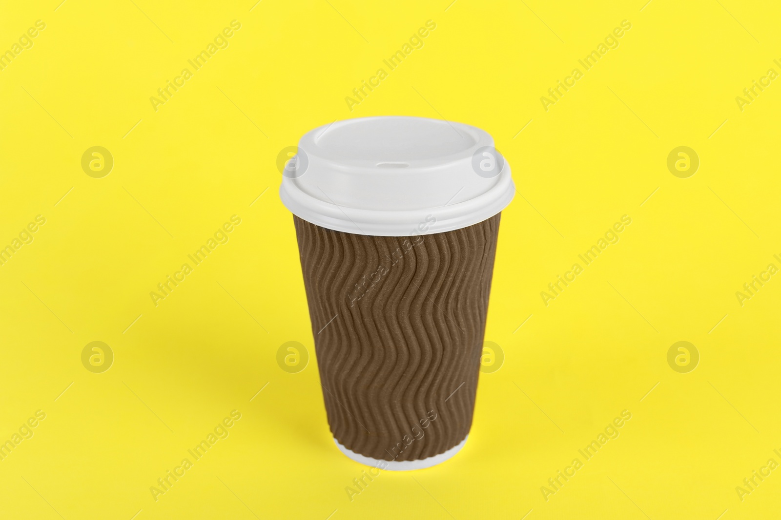 Photo of Brown paper cup with plastic lid on yellow background. Coffee to go