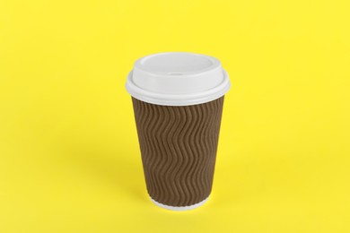 Brown paper cup with plastic lid on yellow background. Coffee to go