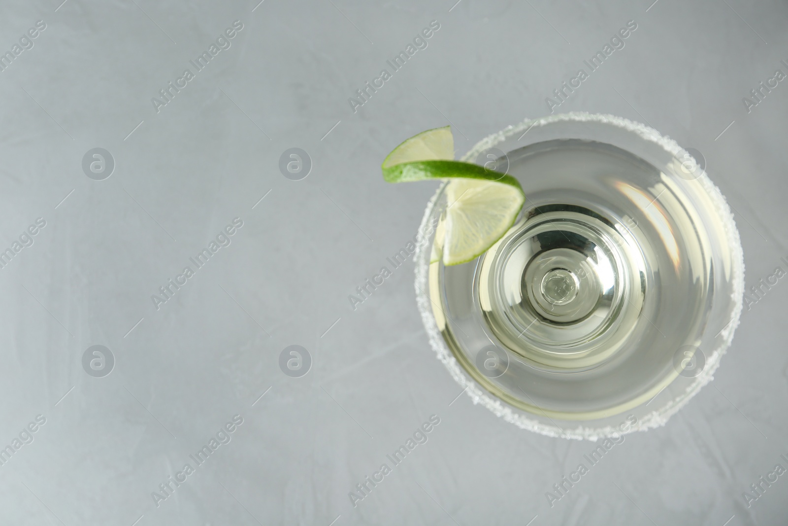 Photo of Glass of lemon drop martini cocktail with lime slice on grey table, top view. Space for text