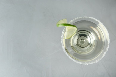 Photo of Glass of lemon drop martini cocktail with lime slice on grey table, top view. Space for text