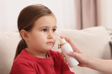 Mother using nasal spray to treat her little daughter on sofa indoors, closeup