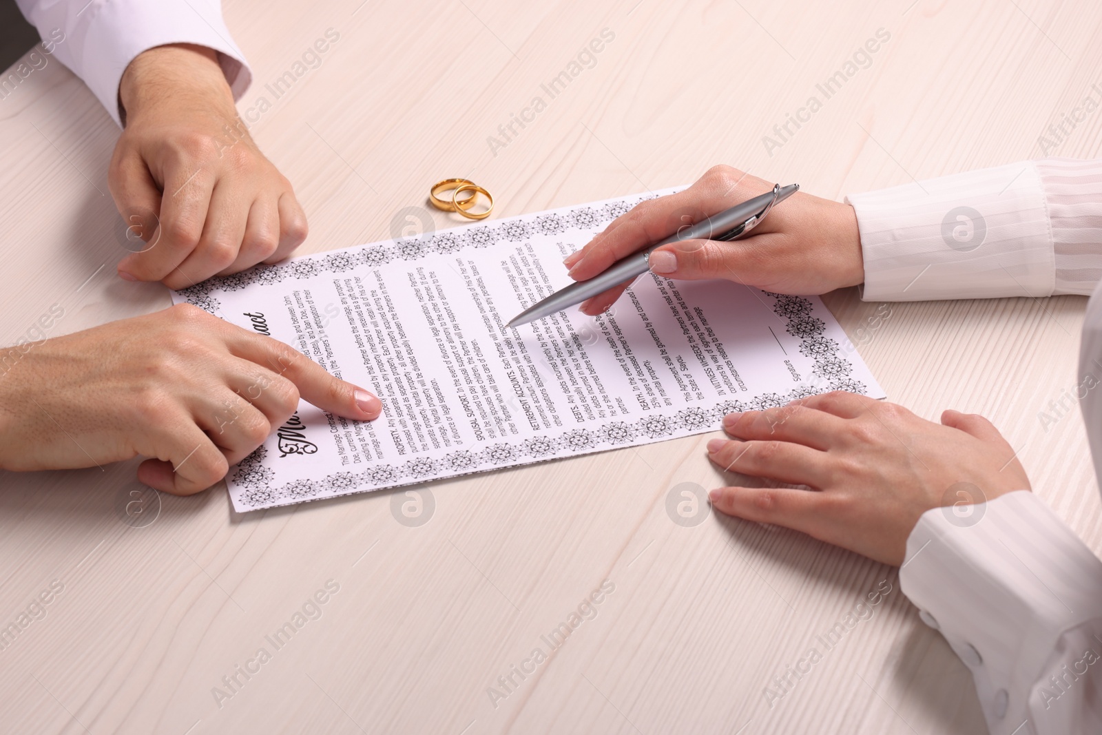 Photo of Man and woman signing marriage contract at light wooden table, closeup