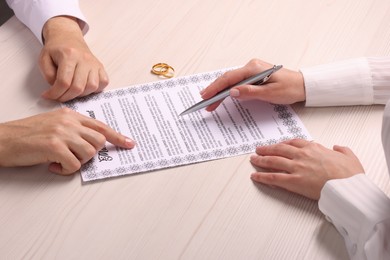 Man and woman signing marriage contract at light wooden table, closeup