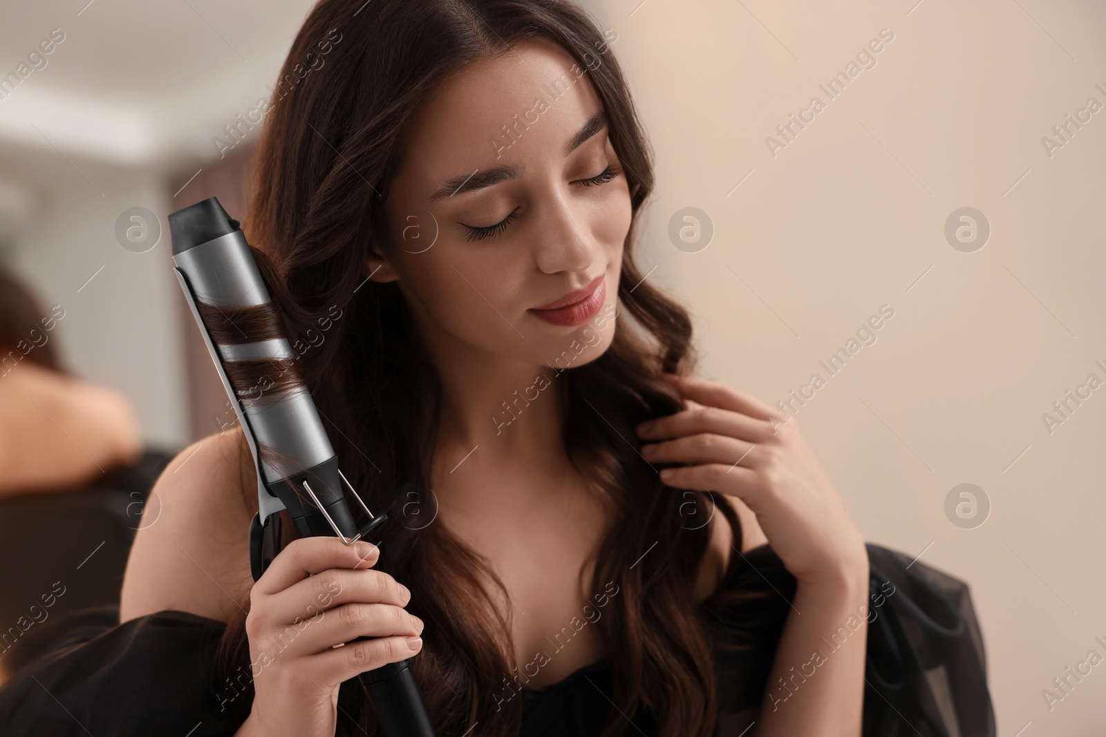 Photo of Beautiful woman using curling hair iron indoors