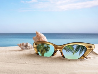 Image of Palms reflecting in sunglasses on sandy beach with seashells near sea