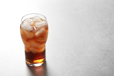 Photo of Glass of cola with ice on light background, space for text