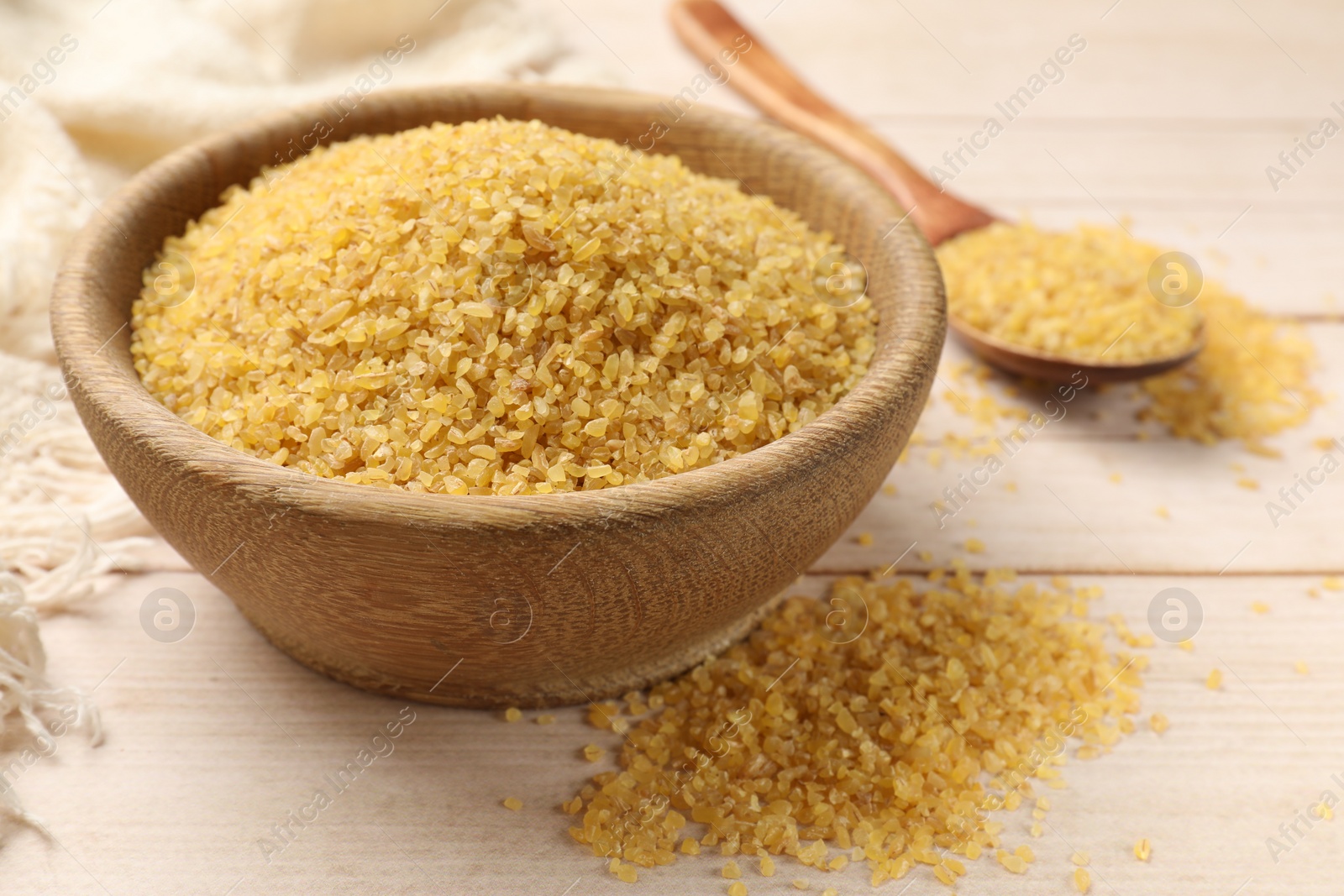 Photo of Bowl and spoon with raw bulgur on light wooden table