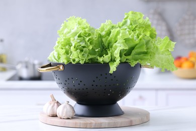 Photo of Fresh lettuce in black colander on white marble table in kitchen, closeup