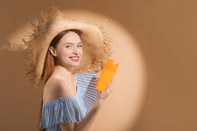 Photo of Beautiful young woman in sunlight holding sun protection cream on beige background, space for text