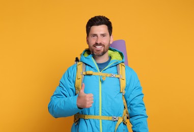 Photo of Happy man with backpack showing thumb up on orange background. Active tourism