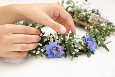 Woman making flower wreath at white wooden table, closeup