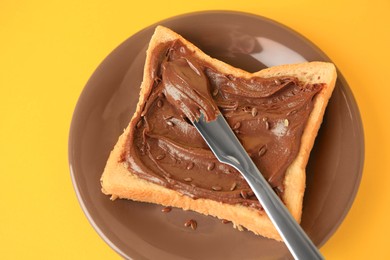 Photo of Spreading chocolate paste onto bread on yellow background, closeup