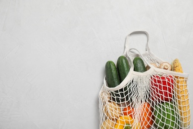 Photo of Mesh bag with fresh vegetables on light grey background, space for text