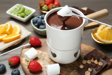 Dipping sweet marshmallow in fondue pot with melted chocolate at wooden table