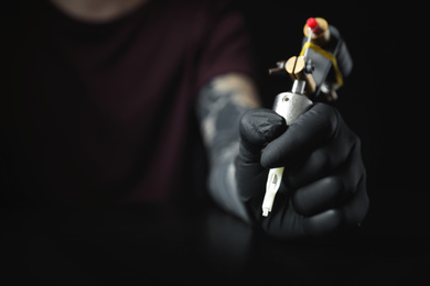 Photo of Tattoo artist with professional machine at table against black background, closeup