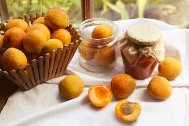 Photo of Jar of delicious jam and fresh ripe apricots on tablecloth indoors. Fruit preserve