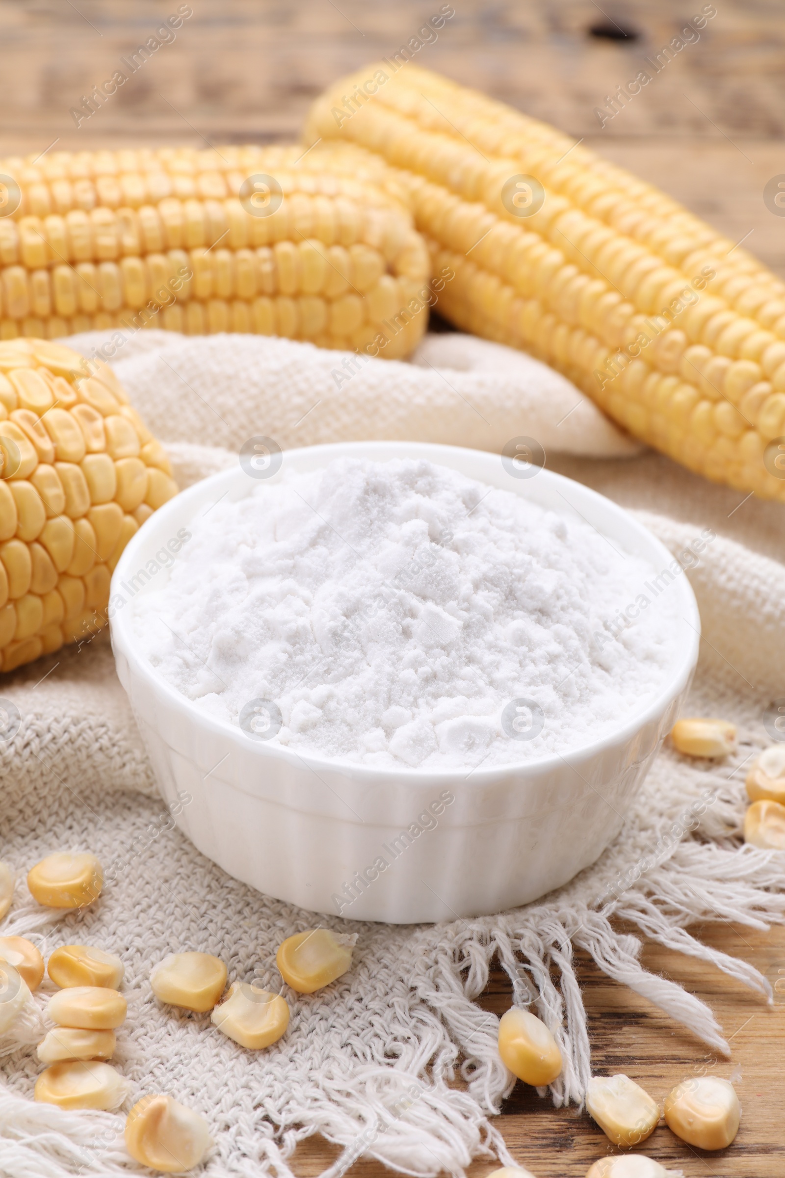 Photo of Bowl with corn starch, ripe cobs and kernels on table