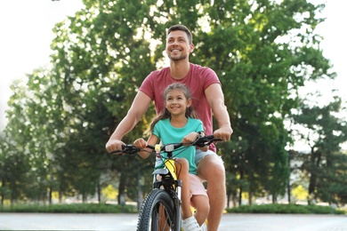 Happy father with daughter riding bicycle in city