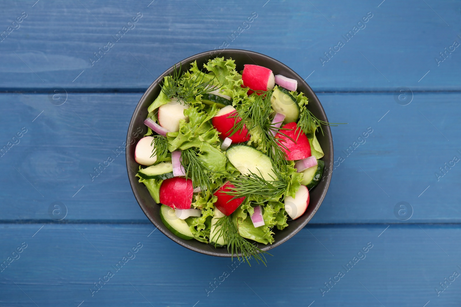 Photo of Tasty salad with radish in bowl on blue wooden table, top view