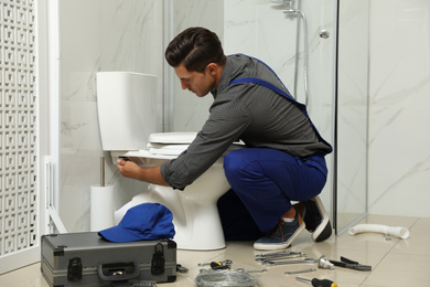 Professional plumber working with toilet bowl in bathroom