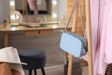 Photo of Clothes rack with light blue bag and pink shirt in makeup room, closeup