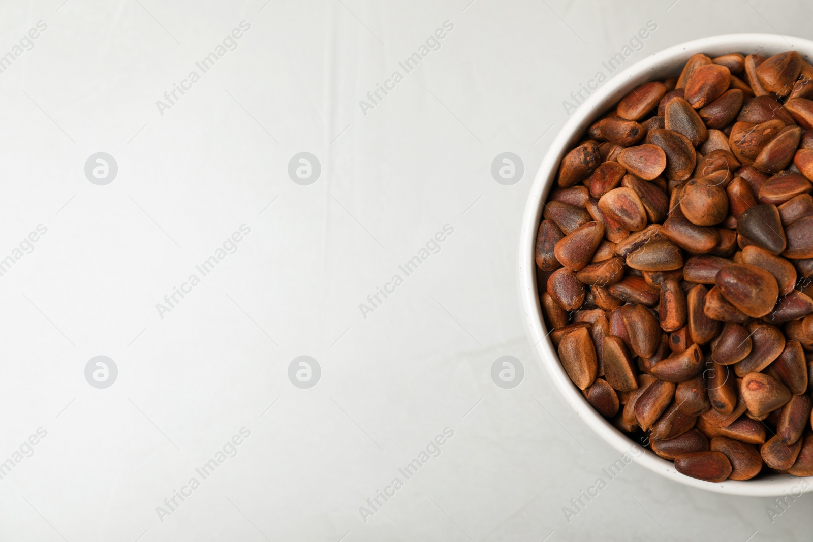 Photo of Bowl with pine nuts on light background, top view. Space for text